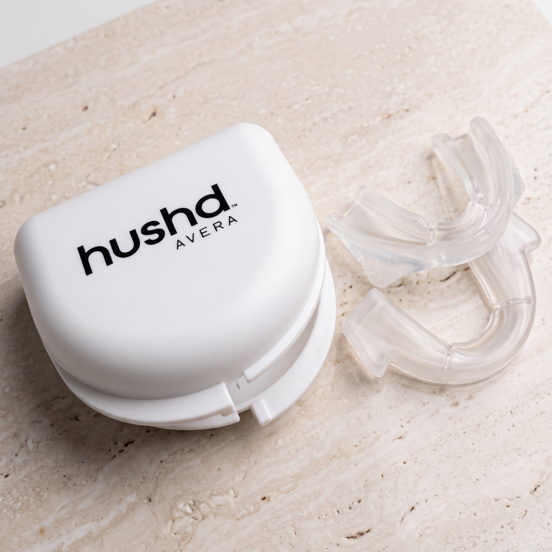 A white hushd Avera mouthpiece case next to a clear silicone mouthpiece on a light beige stone surface.